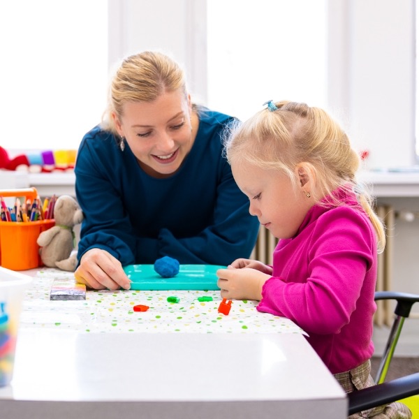 A behaviour analyst and a young girl shaping modelling dough at a table