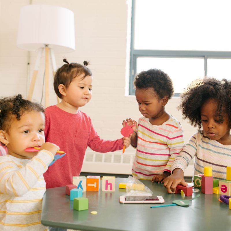 Four young children playing with letter blocks around a table